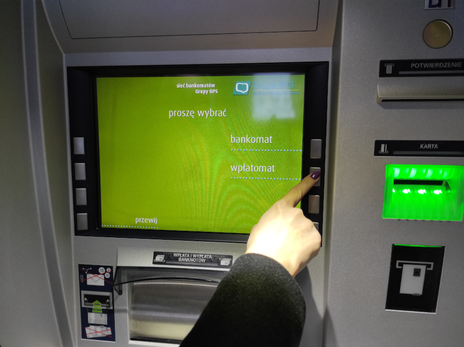 Dłoń wskazująca na przycisk odpowiadający za wybór funkcji wpłatomatu
