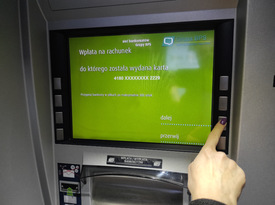 Na ekranie urządzenia przedstawione są informację dotyczące rachunku, na który następuje wpłata. Dłoń wskazuje przycisk odpowiadający na przejście dalej