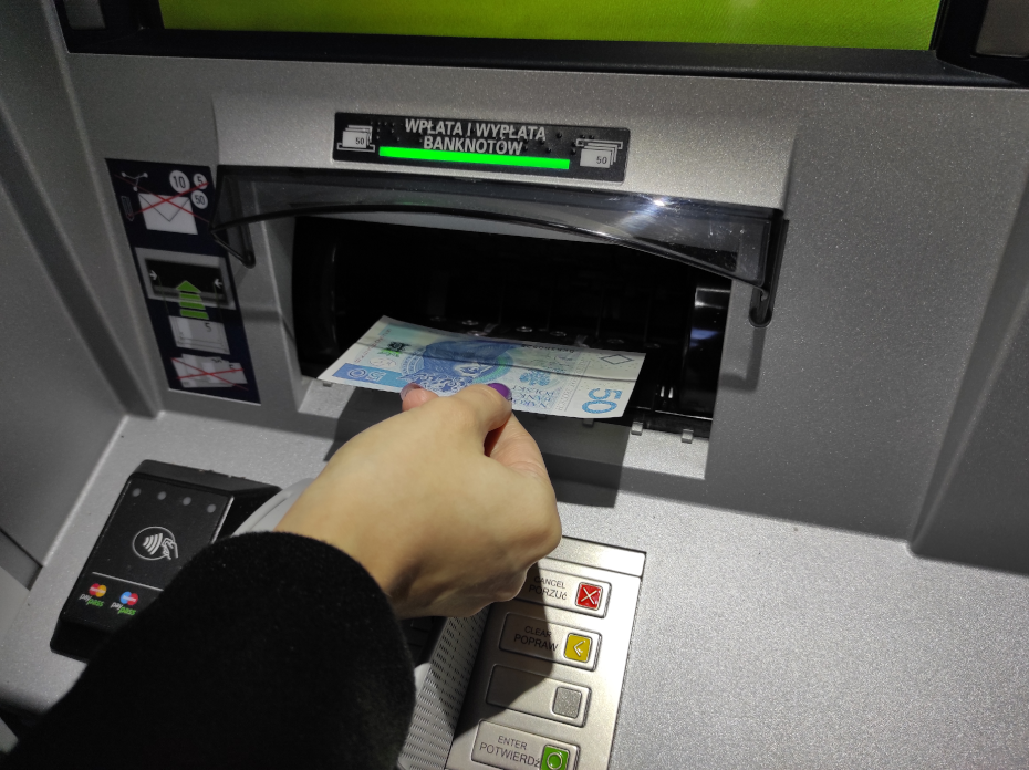 Otwór urządzenia służący do włożenia banknotów, dłoń wkładająca do niego banknot 50 zł