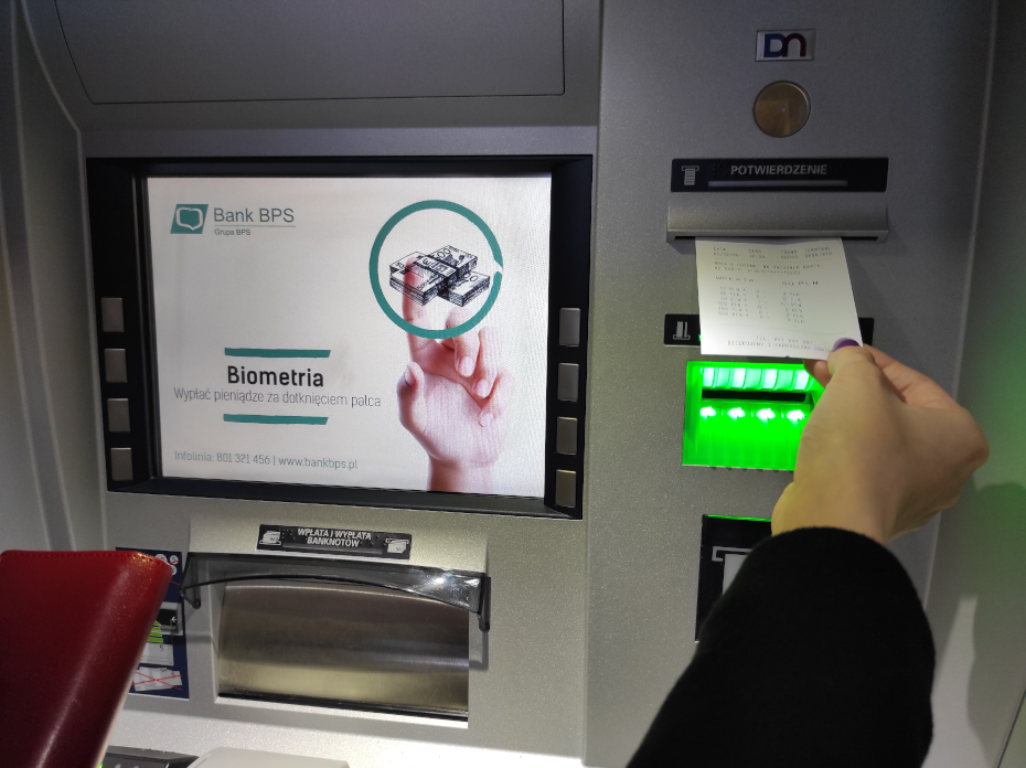 Dłoń wyjmująca potwierdzenie transakcji w formie paragonu z urządzenia